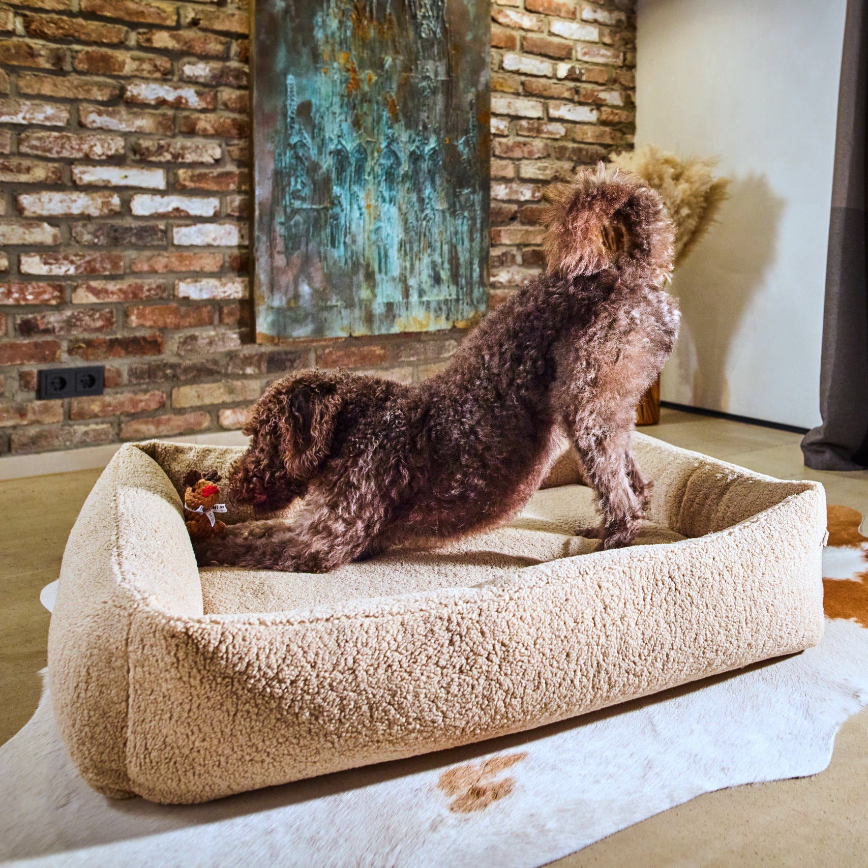 Chien jouant dans son panier beige avec le jouet Rudi le Renne Laboni entre les pattes.