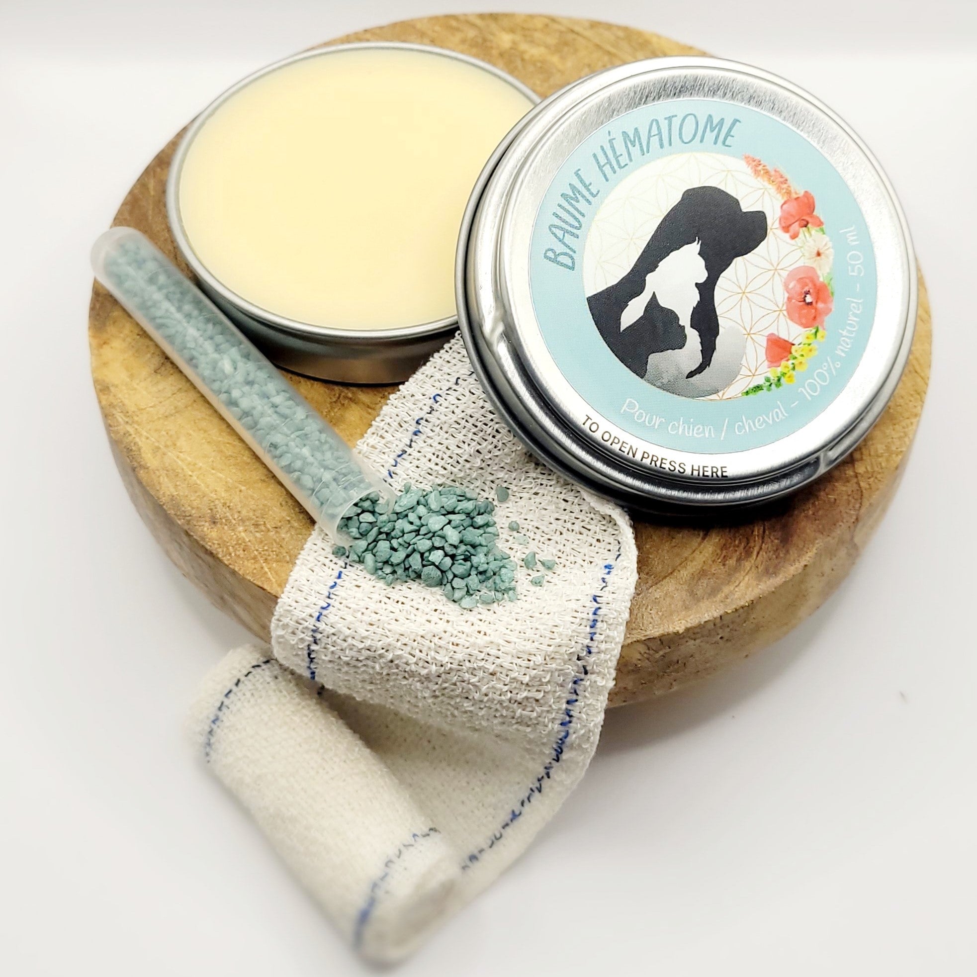 Baume Hématome naturel pour chien et cheval – boîte ouverte avec baume visible, posée sur un support en bois avec bande et granulés verts en décoration.